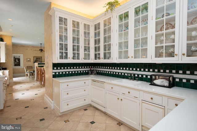 kitchen featuring a sink, white cabinets, white dishwasher, light tile patterned floors, and glass insert cabinets