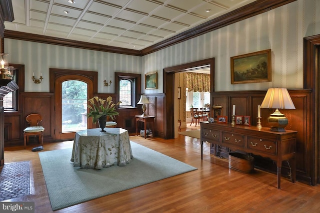 sitting room with ornamental molding, wallpapered walls, an ornate ceiling, wainscoting, and light wood finished floors