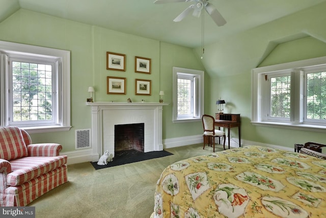 carpeted bedroom featuring vaulted ceiling, a fireplace with flush hearth, baseboards, and visible vents