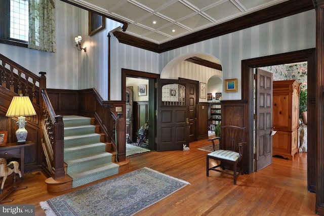 entryway featuring wood finished floors, arched walkways, wainscoting, wallpapered walls, and stairs