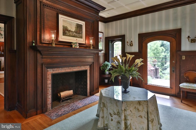 living area with a fireplace with flush hearth, wood finished floors, crown molding, and wallpapered walls