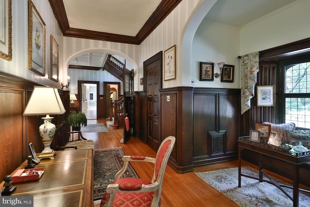 entrance foyer with crown molding, wood finished floors, arched walkways, and wainscoting