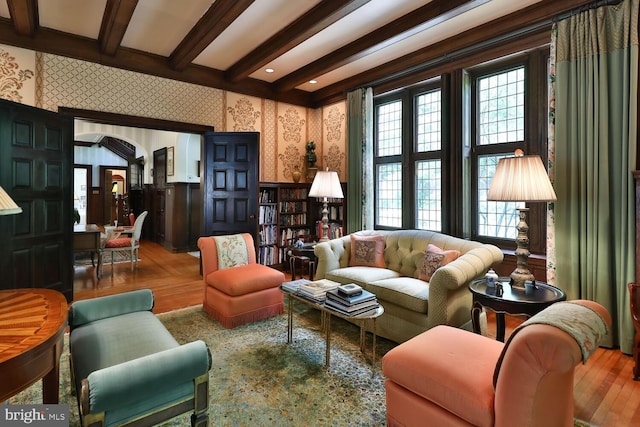 living room featuring wallpapered walls, beamed ceiling, wood finished floors, and a wainscoted wall