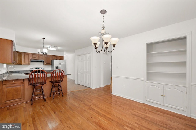 kitchen featuring appliances with stainless steel finishes, light hardwood / wood-style floors, a notable chandelier, and a breakfast bar