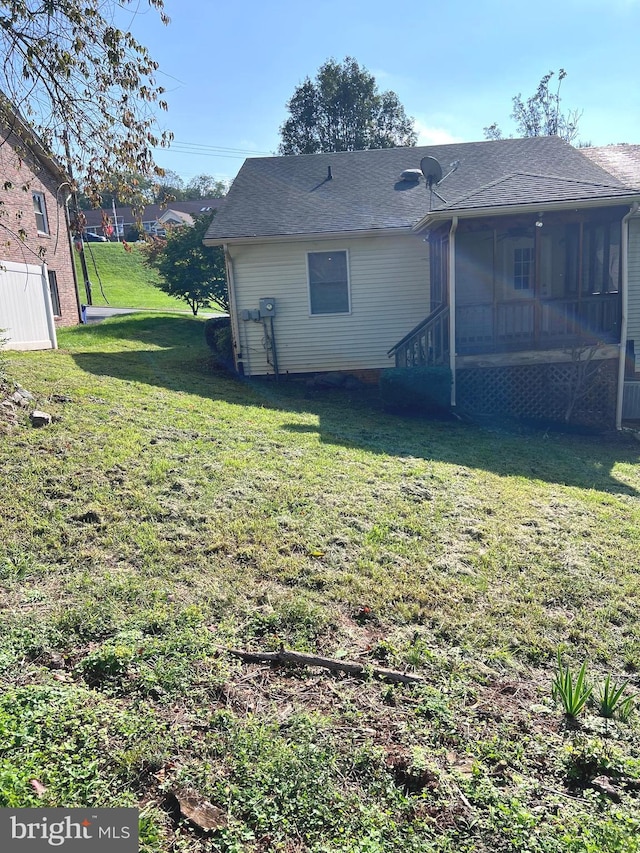 back of property featuring a lawn, a sunroom, and a shingled roof