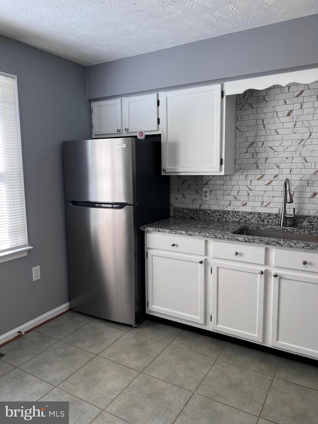 kitchen with a sink, white cabinetry, dark stone countertops, and freestanding refrigerator