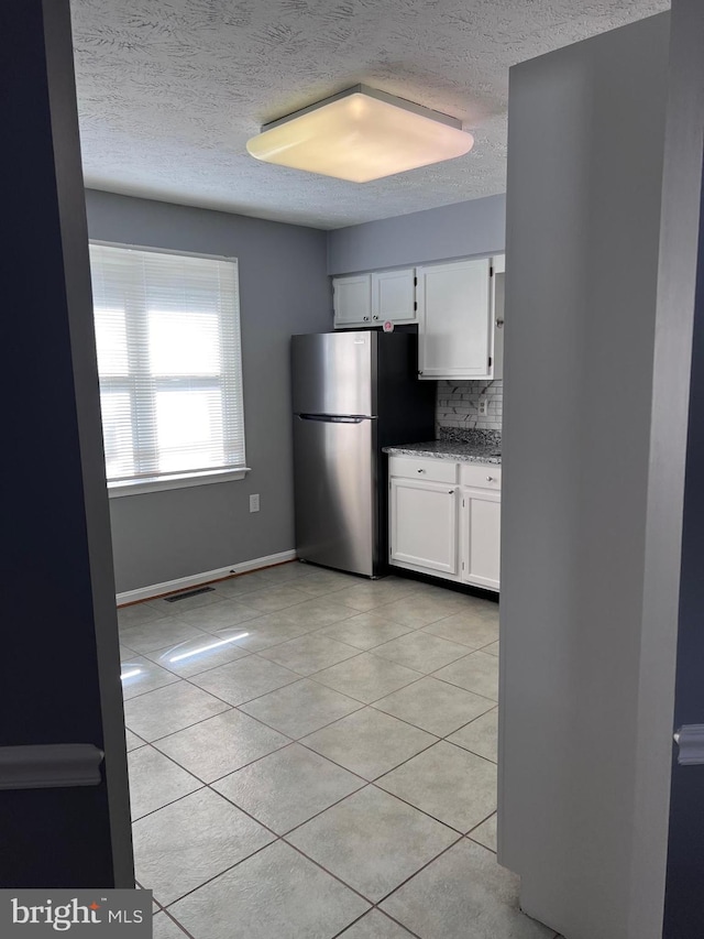 kitchen with backsplash, white cabinetry, light stone countertops, stainless steel refrigerator, and light tile patterned flooring