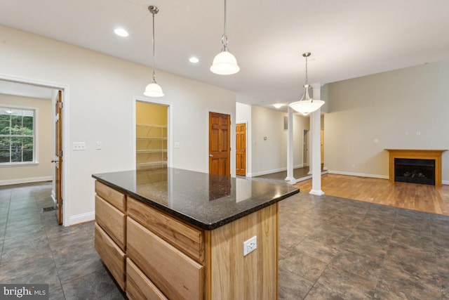 kitchen featuring dark wood-type flooring, pendant lighting, a center island, dark stone counters, and decorative columns