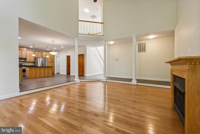 unfurnished living room with light hardwood / wood-style flooring, a towering ceiling, and decorative columns