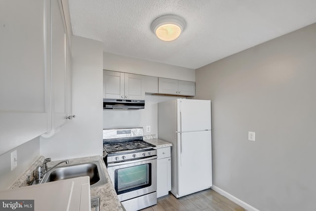 kitchen with white refrigerator, sink, a textured ceiling, stainless steel range with gas cooktop, and light hardwood / wood-style floors