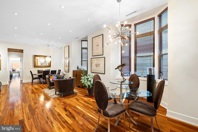 dining space with a wealth of natural light, hardwood / wood-style floors, and an inviting chandelier