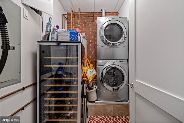 washroom with laundry area, beverage cooler, stacked washer and clothes dryer, and brick wall