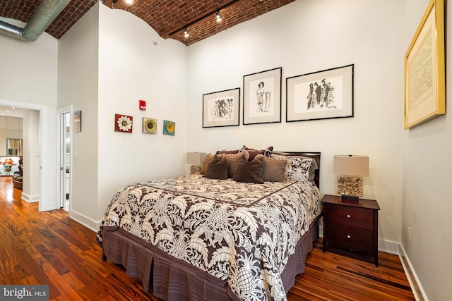 bedroom featuring dark wood-type flooring, track lighting, and a towering ceiling