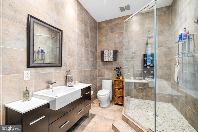 bathroom with a shower with door, vanity, toilet, and tile walls