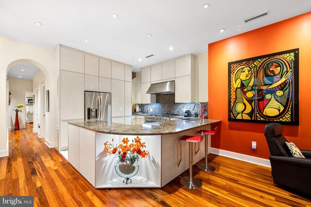 kitchen featuring appliances with stainless steel finishes, light hardwood / wood-style floors, dark stone counters, a kitchen breakfast bar, and tasteful backsplash