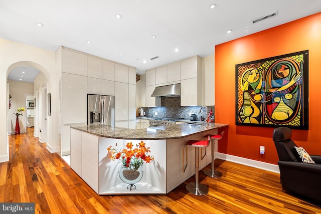 kitchen with visible vents, under cabinet range hood, dark stone counters, appliances with stainless steel finishes, and a peninsula