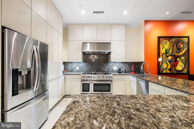 kitchen featuring range hood, dark stone countertops, stainless steel appliances, sink, and kitchen peninsula