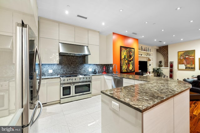 kitchen with appliances with stainless steel finishes, tasteful backsplash, kitchen peninsula, sink, and dark stone countertops