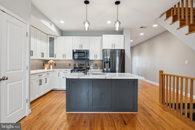 kitchen featuring backsplash, light wood-type flooring, light stone countertops, stainless steel appliances, and white cabinetry