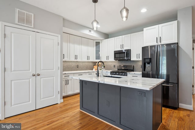 kitchen featuring a kitchen island with sink, pendant lighting, stainless steel appliances, white cabinets, and light hardwood / wood-style floors