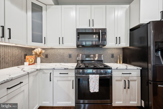 kitchen with light stone countertops, backsplash, stainless steel appliances, and white cabinets