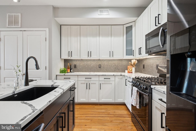 kitchen featuring white cabinets, appliances with stainless steel finishes, backsplash, and light hardwood / wood-style flooring