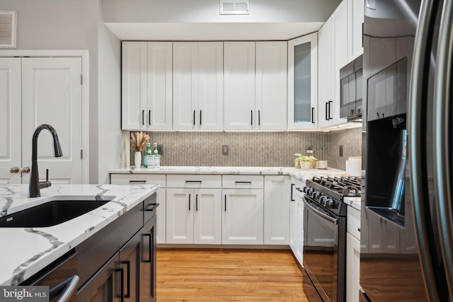 kitchen featuring white cabinetry, light hardwood / wood-style flooring, tasteful backsplash, sink, and appliances with stainless steel finishes