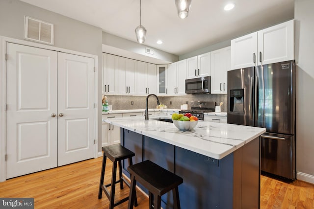 kitchen featuring light hardwood / wood-style flooring, an island with sink, hanging light fixtures, stainless steel appliances, and sink