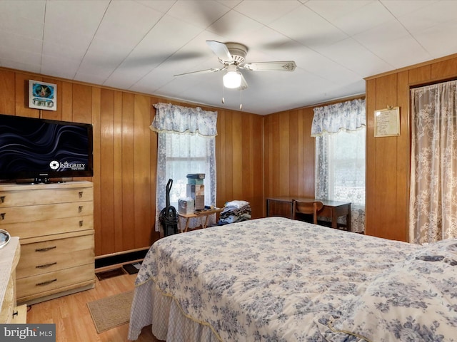 bedroom with wood walls, light hardwood / wood-style floors, multiple windows, and ceiling fan