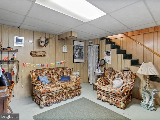 living room featuring a paneled ceiling, wood walls, and concrete flooring