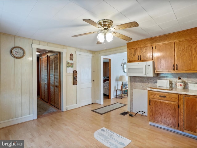 kitchen featuring wood walls, backsplash, light wood-type flooring, and ceiling fan