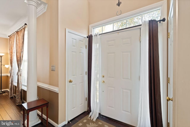 foyer entrance featuring ornate columns, dark hardwood / wood-style flooring, and crown molding