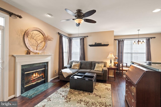 living room featuring ceiling fan with notable chandelier, dark hardwood / wood-style flooring, a high end fireplace, and plenty of natural light