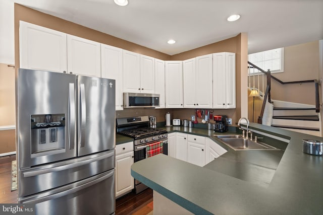 kitchen featuring stainless steel appliances, dark hardwood / wood-style flooring, kitchen peninsula, sink, and white cabinetry