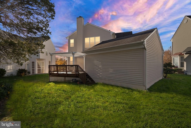 back house at dusk with a pergola, a lawn, and a deck