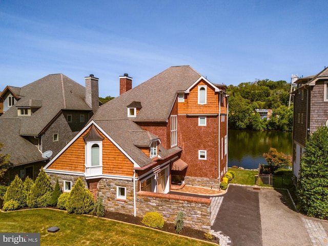 view of front of house with driveway, roof with shingles, a chimney, a front lawn, and a water view