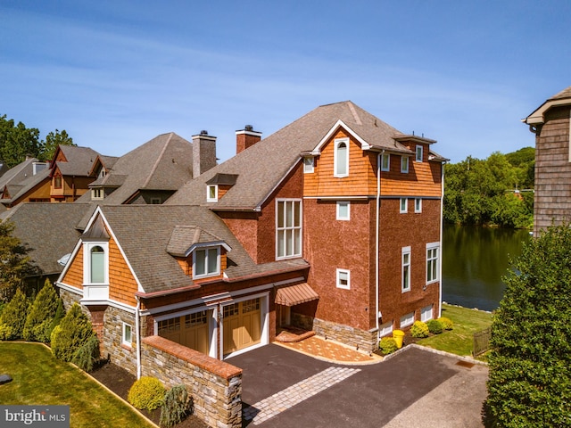 view of front facade featuring driveway, a chimney, a shingled roof, a water view, and stone siding