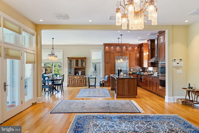 interior space featuring stainless steel built in refrigerator, light hardwood / wood-style floors, wall chimney exhaust hood, pendant lighting, and a kitchen island