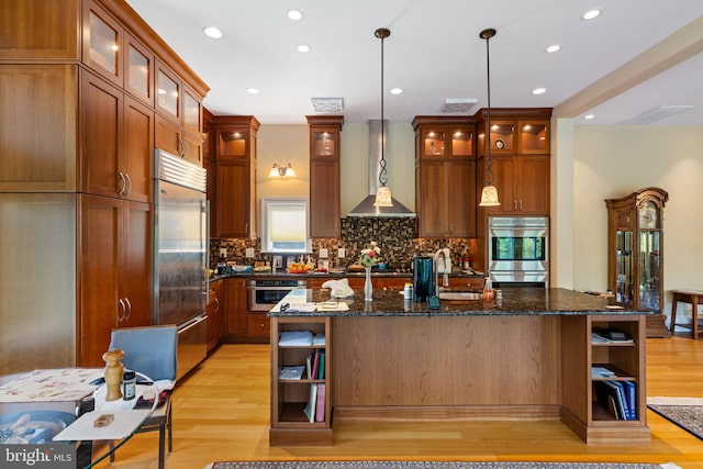 kitchen featuring a center island, light hardwood / wood-style flooring, stainless steel appliances, wall chimney exhaust hood, and pendant lighting