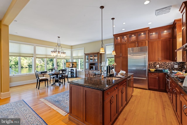 kitchen featuring dark stone countertops, a chandelier, decorative light fixtures, stainless steel appliances, and light hardwood / wood-style floors