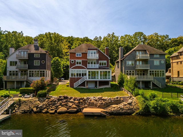 back of house featuring a balcony, a sunroom, a lawn, and a water view