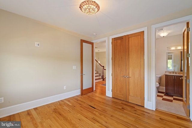 unfurnished bedroom featuring sink, a closet, light hardwood / wood-style floors, and ensuite bath