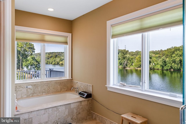 bathroom featuring tiled tub, a healthy amount of sunlight, and a water view