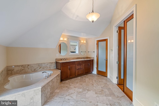 bathroom featuring vanity, vaulted ceiling, and a relaxing tiled tub