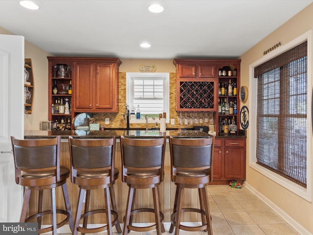 bar with light tile patterned floors, decorative backsplash, and dark stone counters