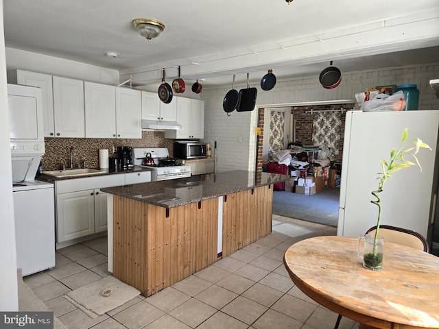 kitchen with stacked washing maching and dryer, white cabinetry, sink, white appliances, and a center island