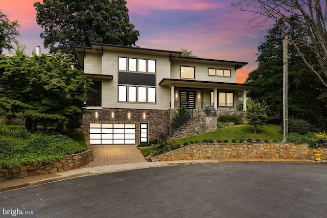 view of front facade with a porch, stone siding, an attached garage, and decorative driveway