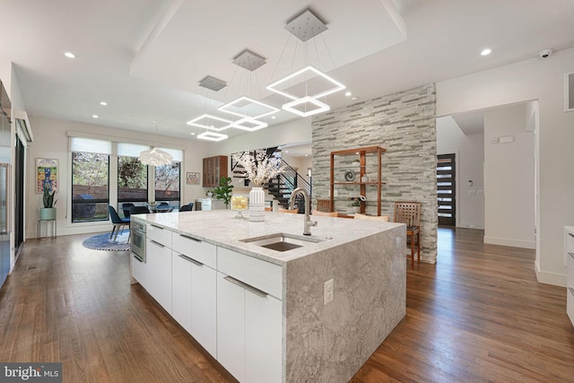 kitchen featuring dark wood-style floors, modern cabinets, a kitchen island with sink, and a sink