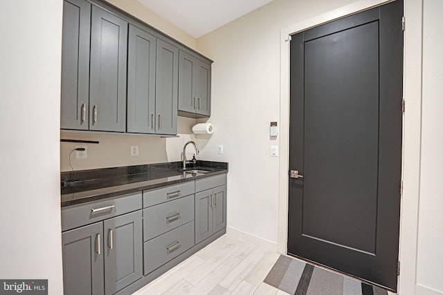 kitchen with baseboards, dark stone counters, gray cabinets, a sink, and light wood-type flooring