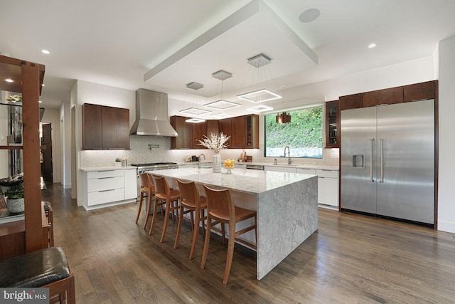 kitchen with a sink, stainless steel appliances, dark wood finished floors, and wall chimney range hood